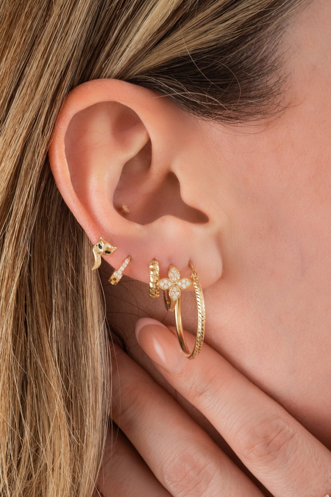 Huggie de oro sólido en 10 kilates con flor de cuatro pétalos tupida de zirconias.