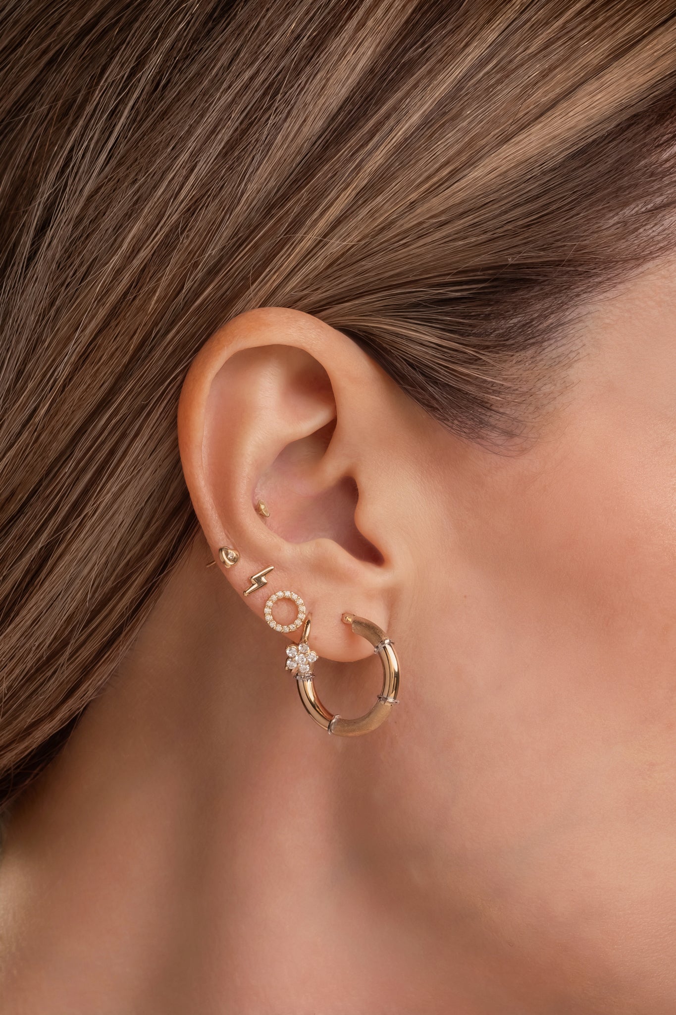 Huggie de oro sólido en 14 kilates con flor de zirconias blancas pétalos picudos.