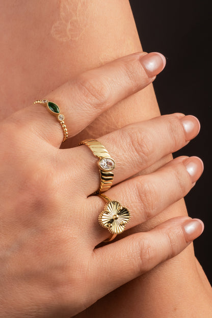 Anillo de oro sólido en 10 kilates con zirconia en forma de semilla verde y dos zirconias circulares a los lados y brazo de bolitas lisas.